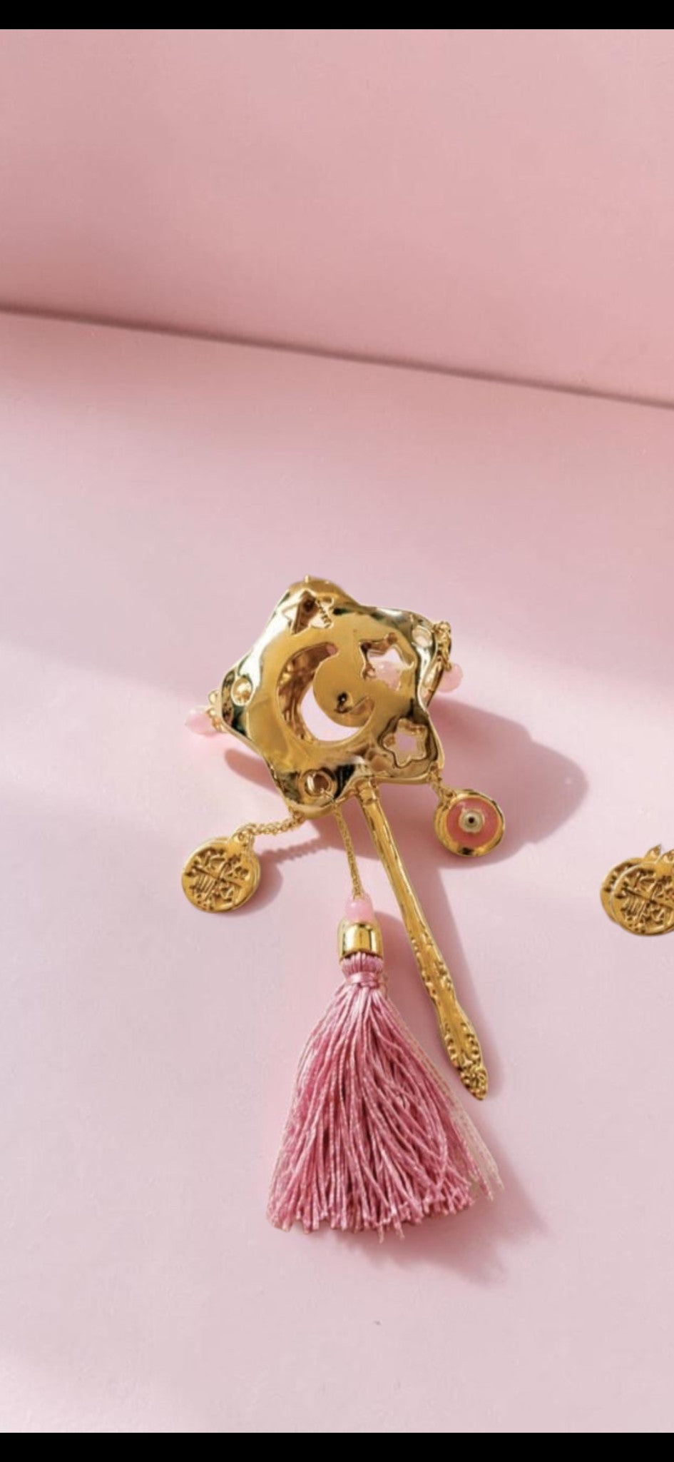 Fina Jewellery gold-tone star keepsake pin with a dusty pink tassel, evil eye bead, and decorative coin charms.